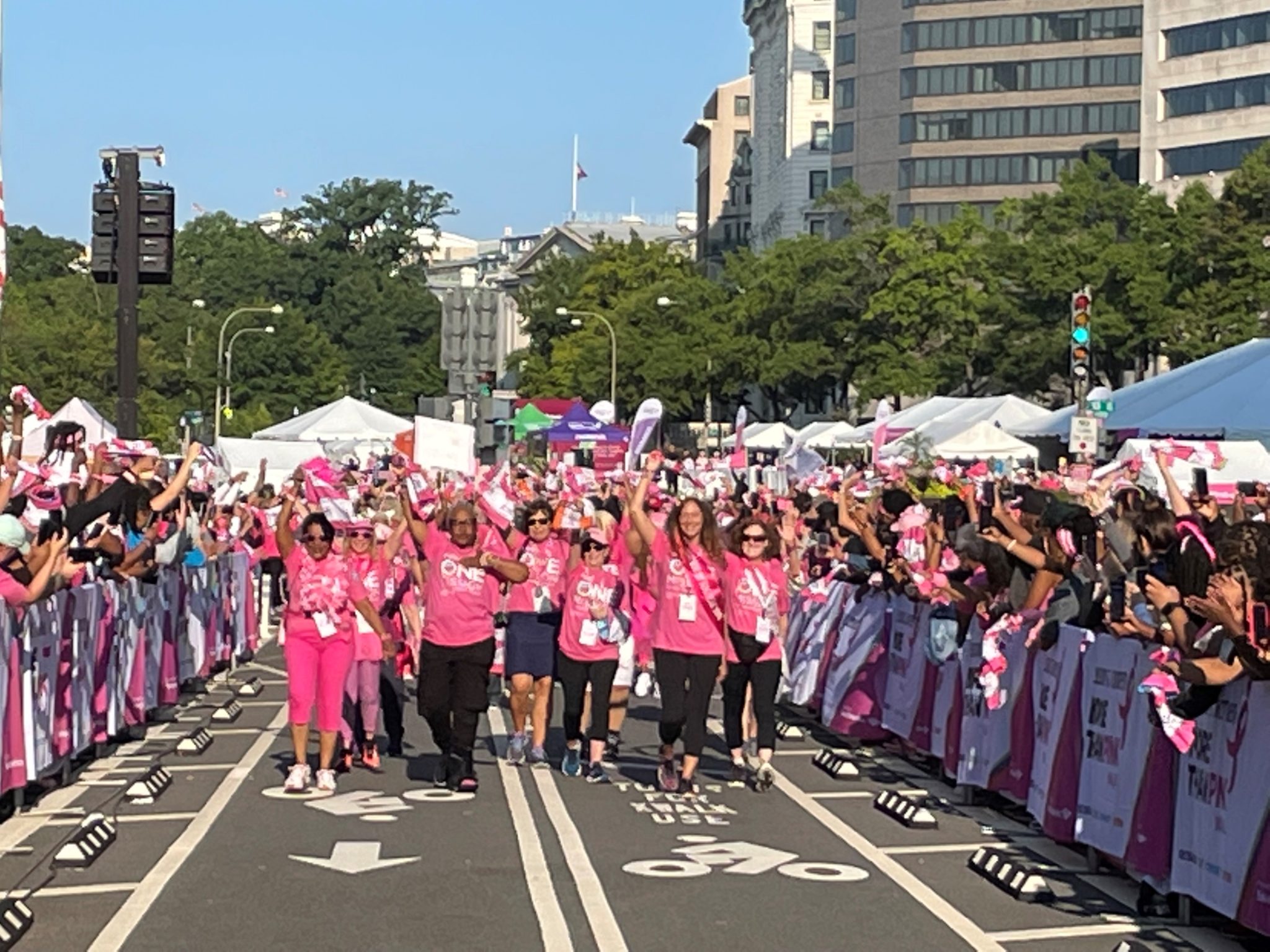 hundreds of people in pink t shirts walk down a DC street waving their hands in the air