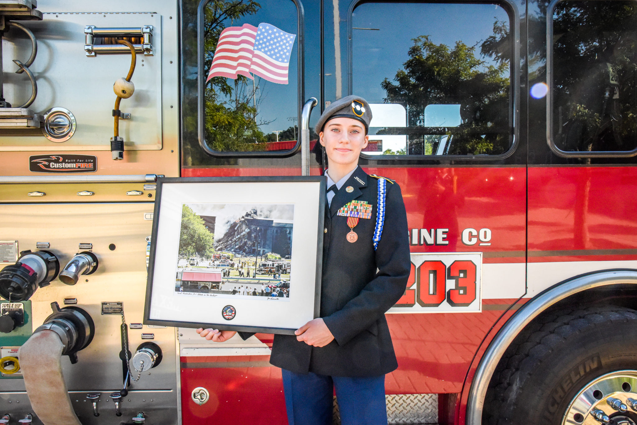 an Alexandria City High School ROTC member holds a framed photo of a 9/11 scene in front of an Alexandria Fire engine