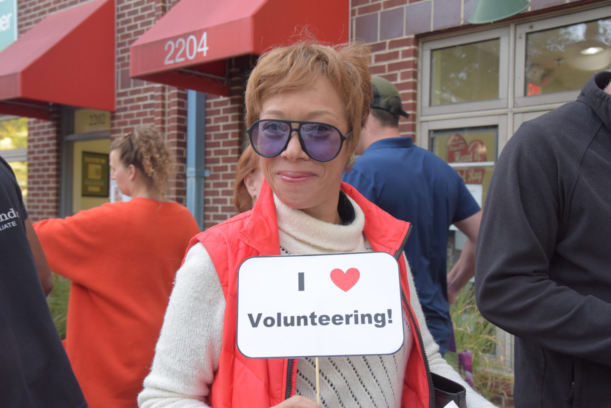 a woman in a red vest holds up a sign that reads "I love volunteering"