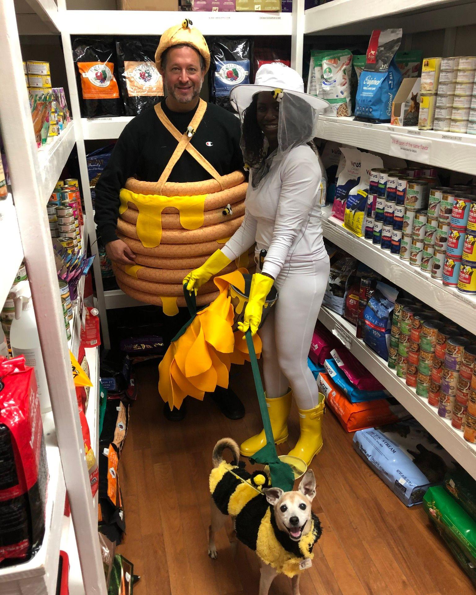 a woman dressed as a bee keeper, holding her dog dressed as a bee, standing next to man dressed as honey pot