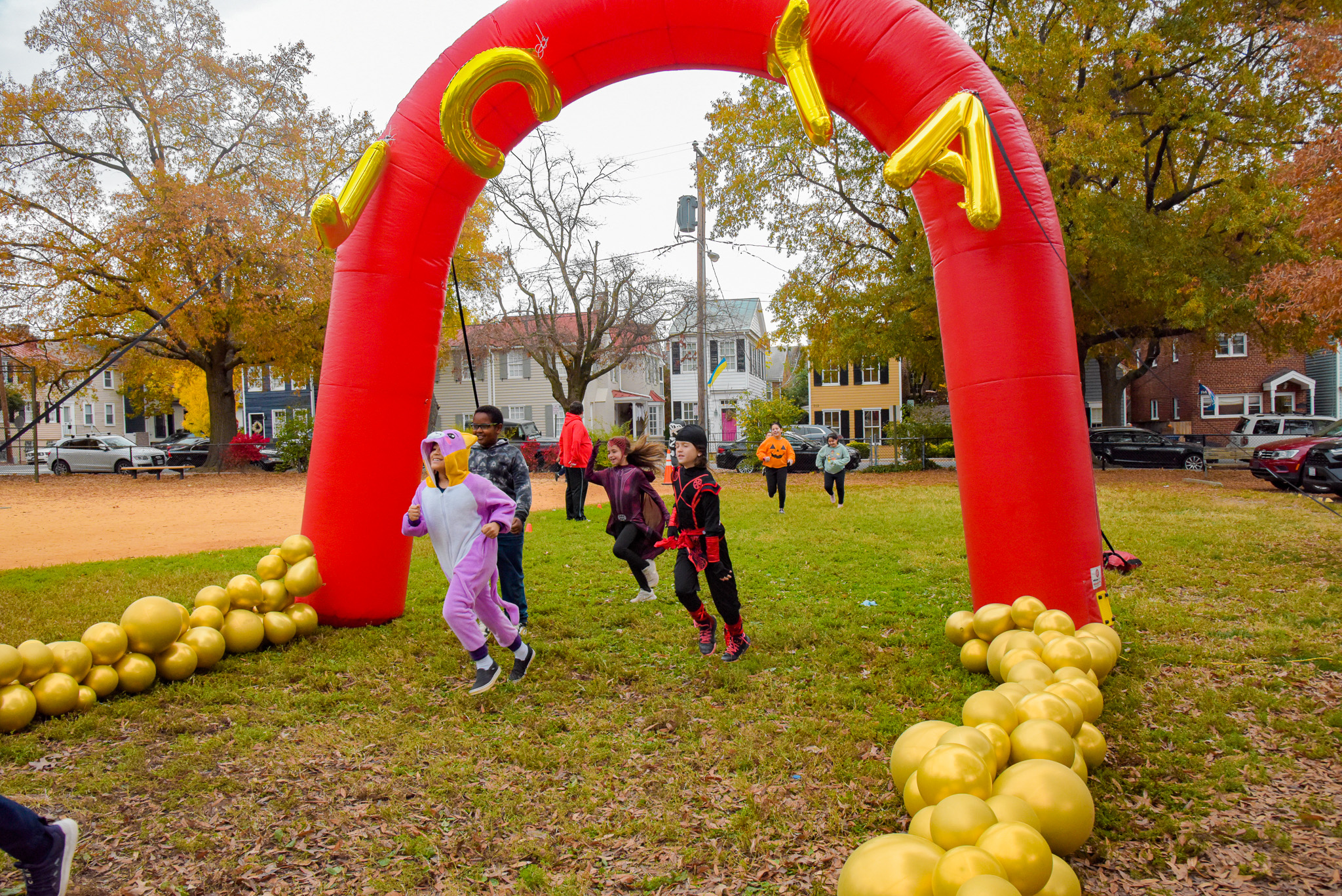 students dressed in halloween costumes run underneath balloon arch