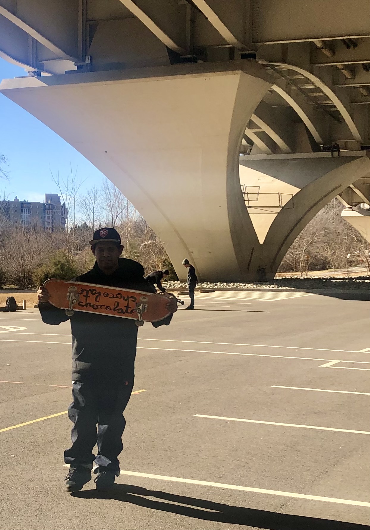 man holding up skateboard under the bridge