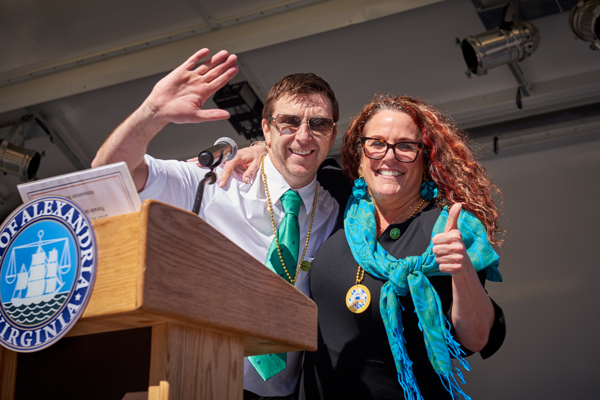 Man and woman smiling and waving from podium wearing green.