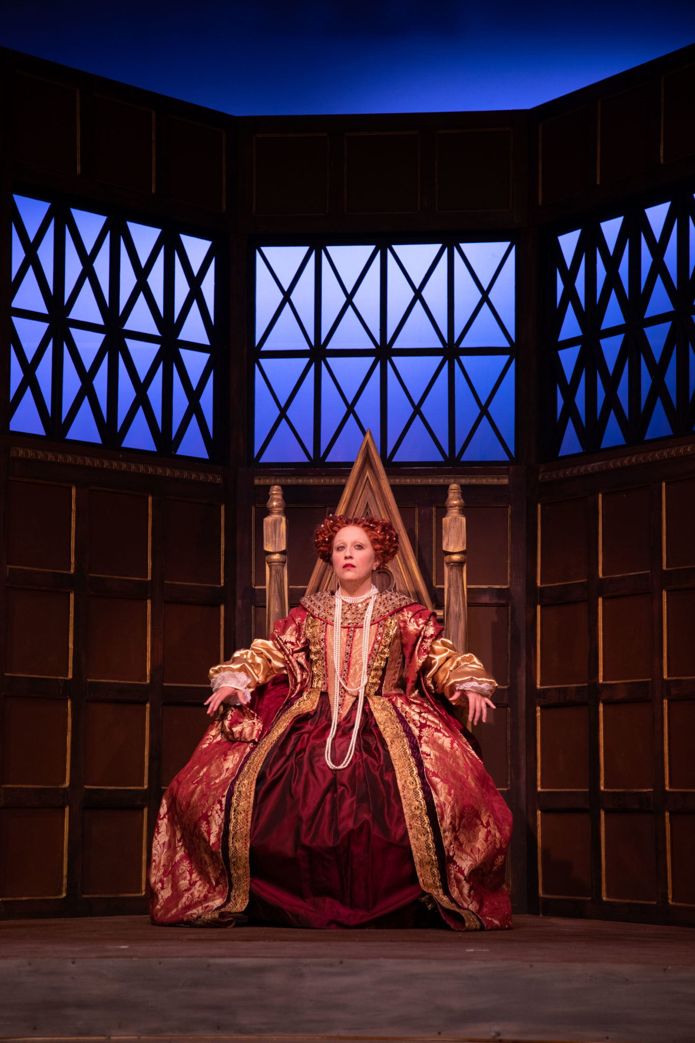 Middle-aged woman in Elizabethean costume on throne.