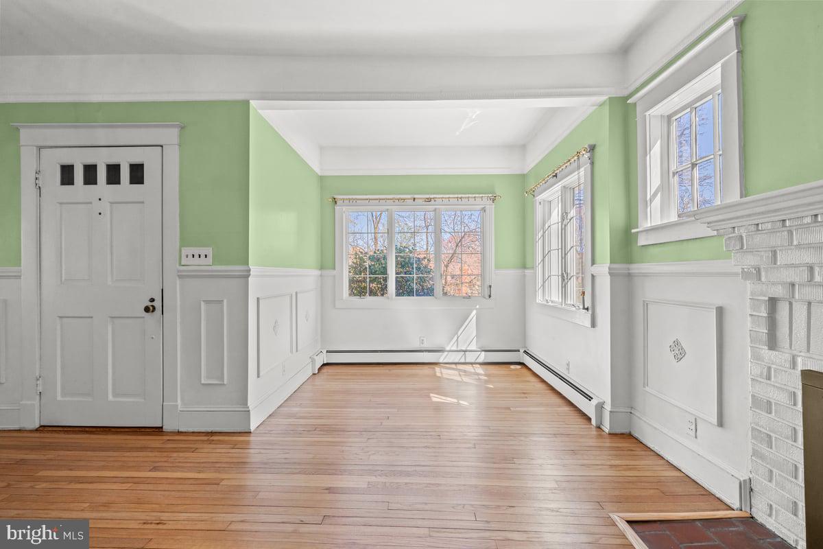 Vacant room in older home with wood floors, green walls and white wainscotting and ireplace.