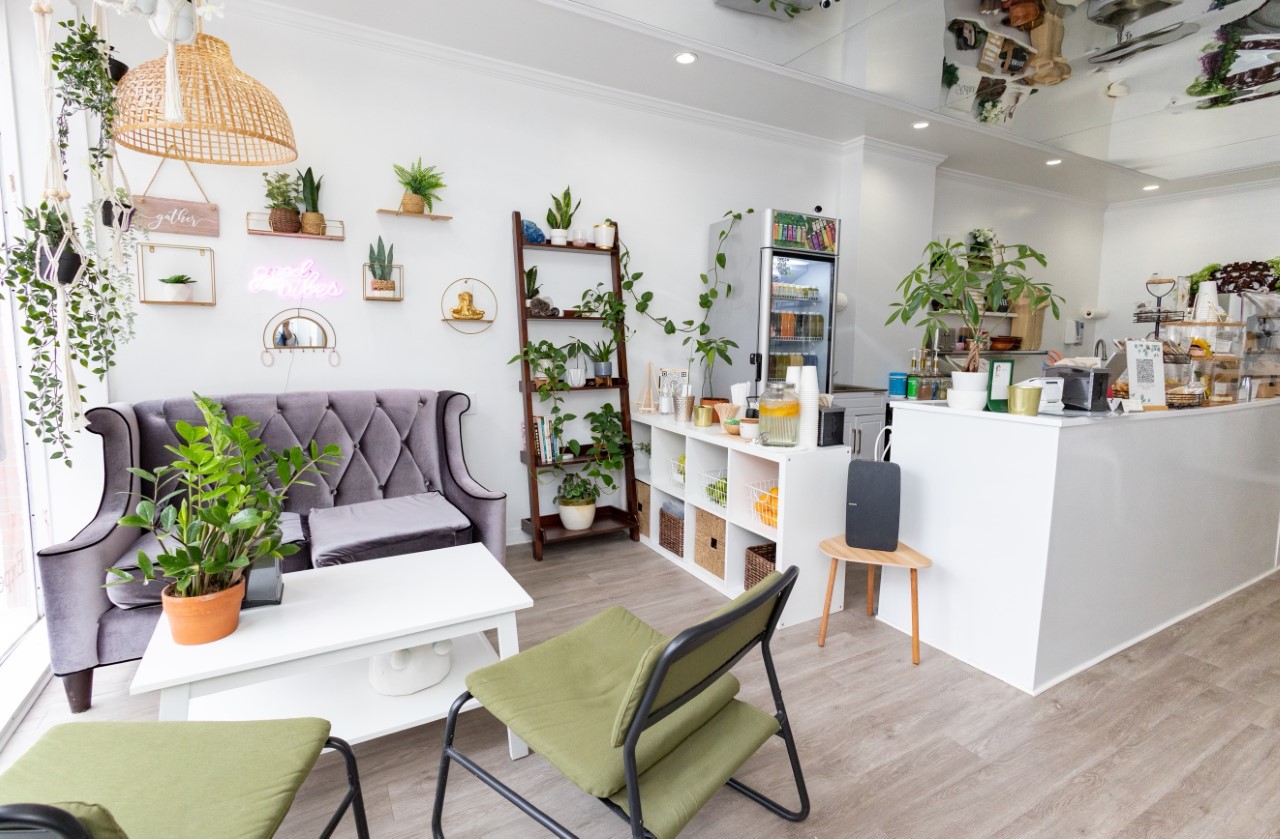 Bright and clean restaurant space with whit floors and tables and green chairs and plants.