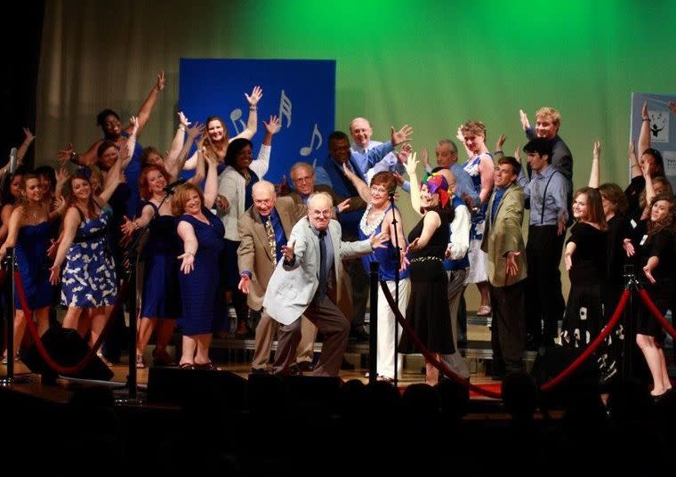 group of men and women in costume with hands raised as in finish of a musical number