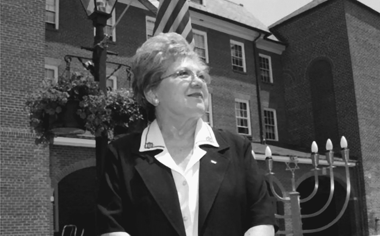 Black and white photo of middle-aged lady looing upward, American flag flying in background behind her.