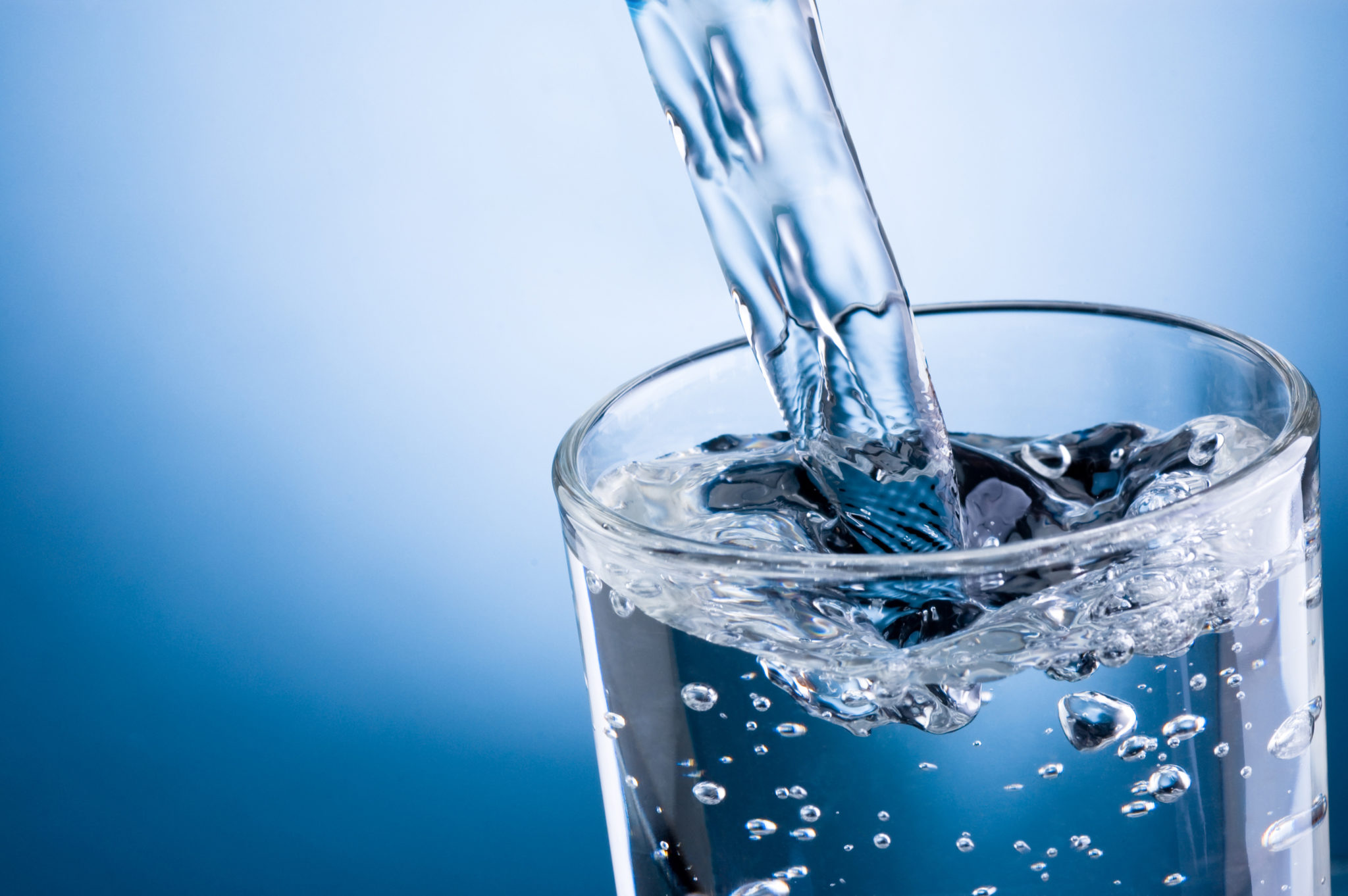 Water pouring into aa glass against blue background.