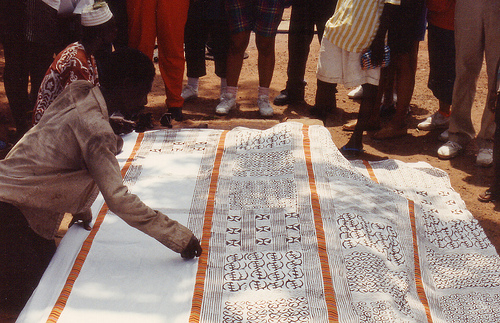 A man is painting a piece of cloth applying symbols.