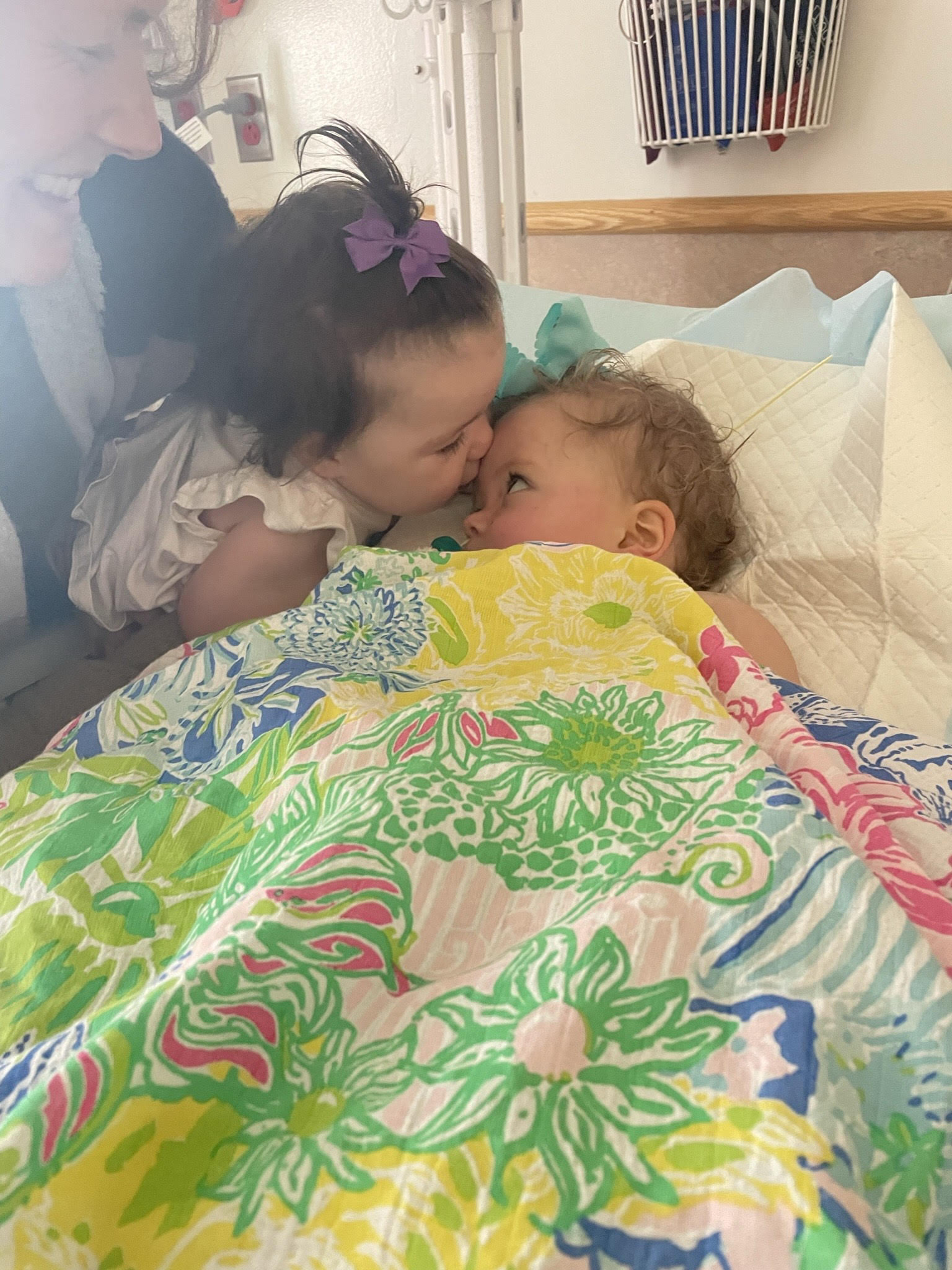 Two infants in hospital bed, one kissing the other.