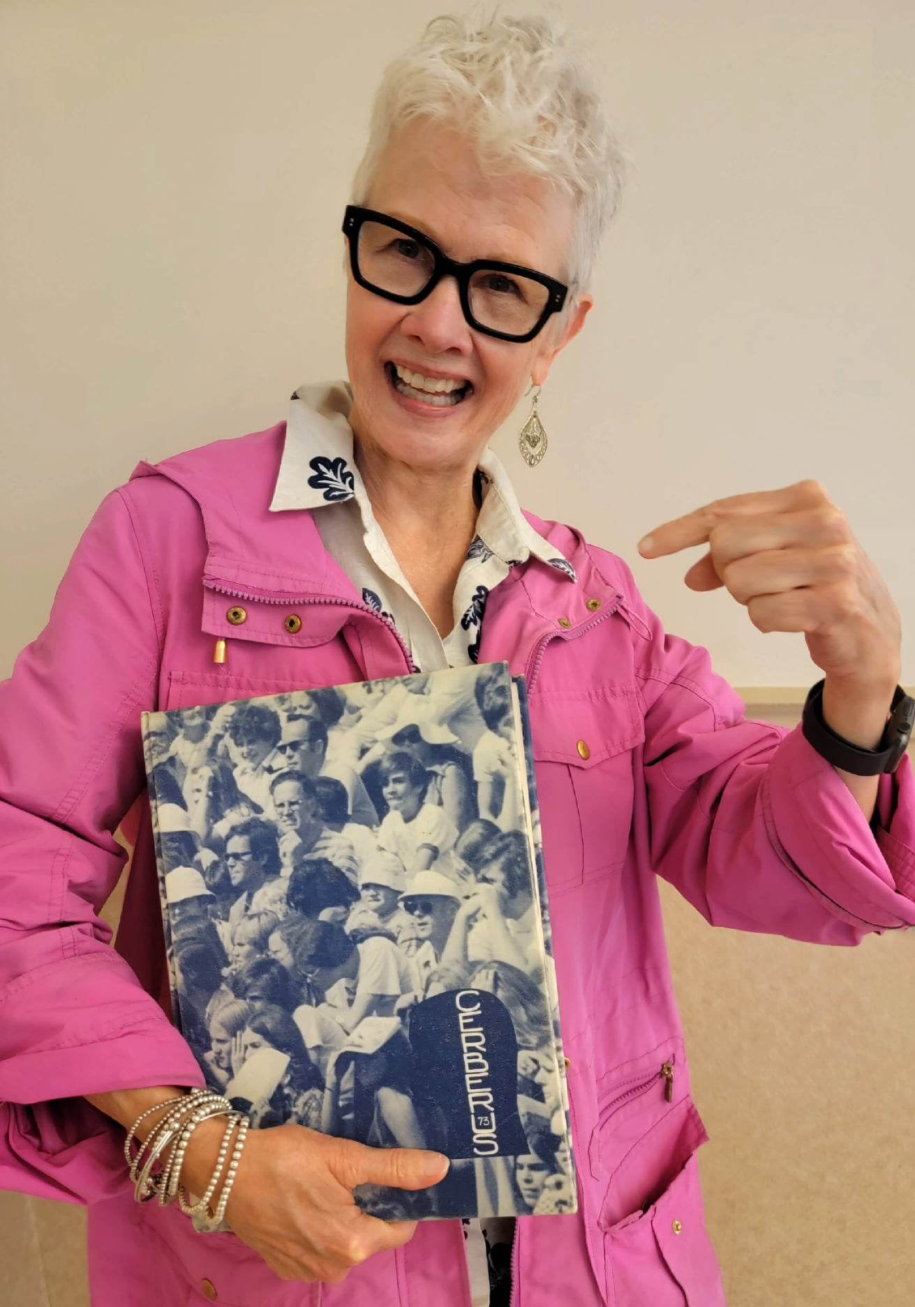 Older lady in pink jacket holds yearbook