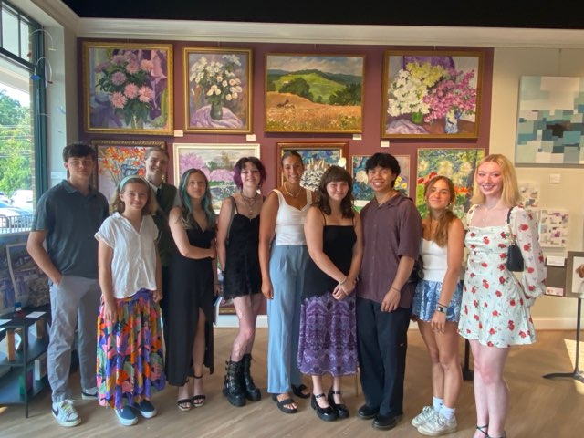 Group of students with artwork on wall behind them.