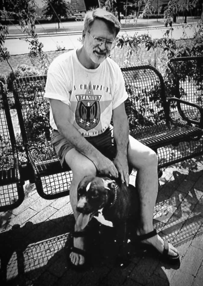 Man sitting on bench petting large black and white dog sitting at his feet. (Photo: Nina Tisara)