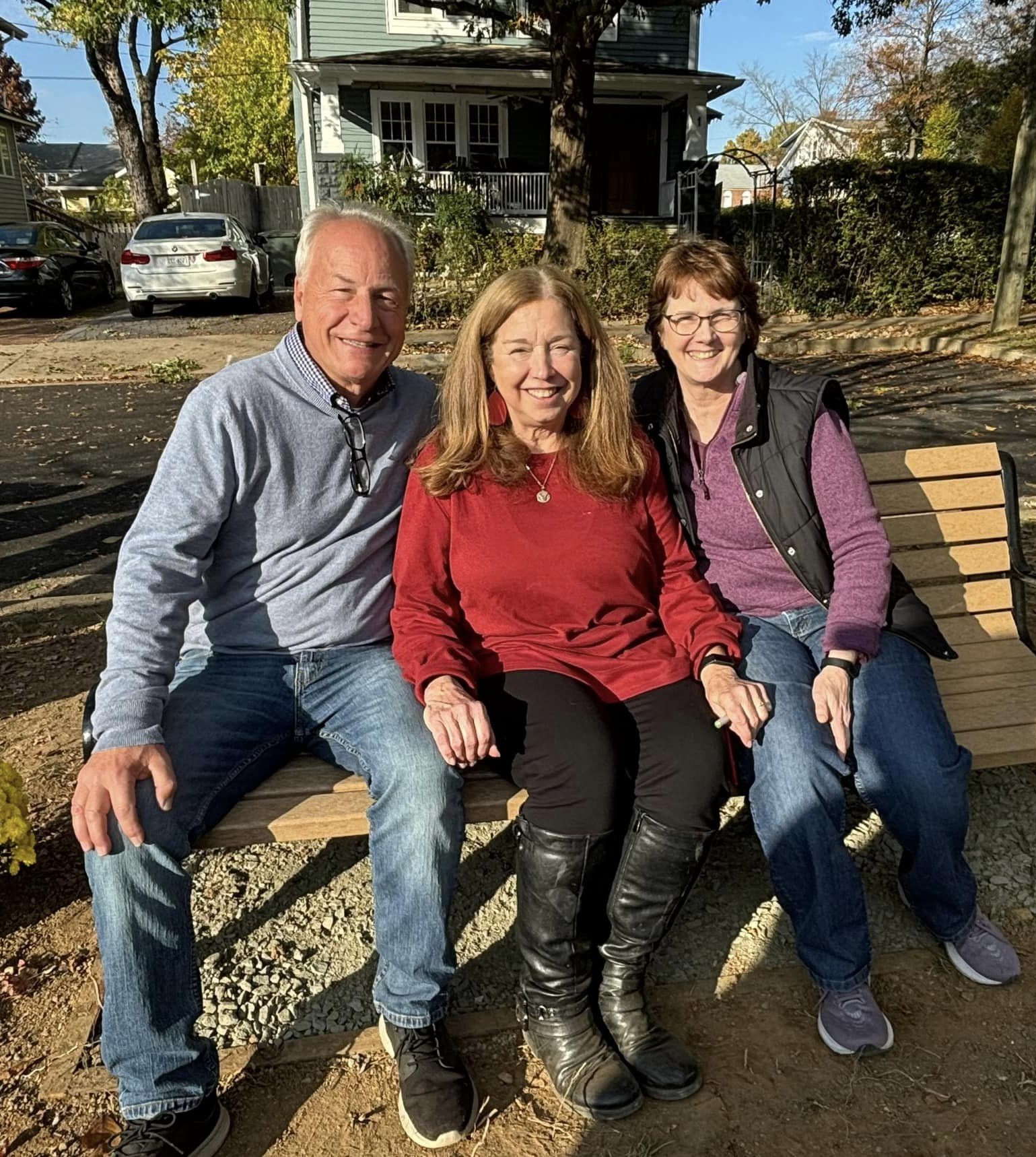 Two women and a man on a bench in front of a house.