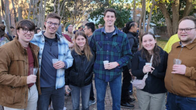 Six people dressed in fall clothing holding cider glasses and smiling at camera.