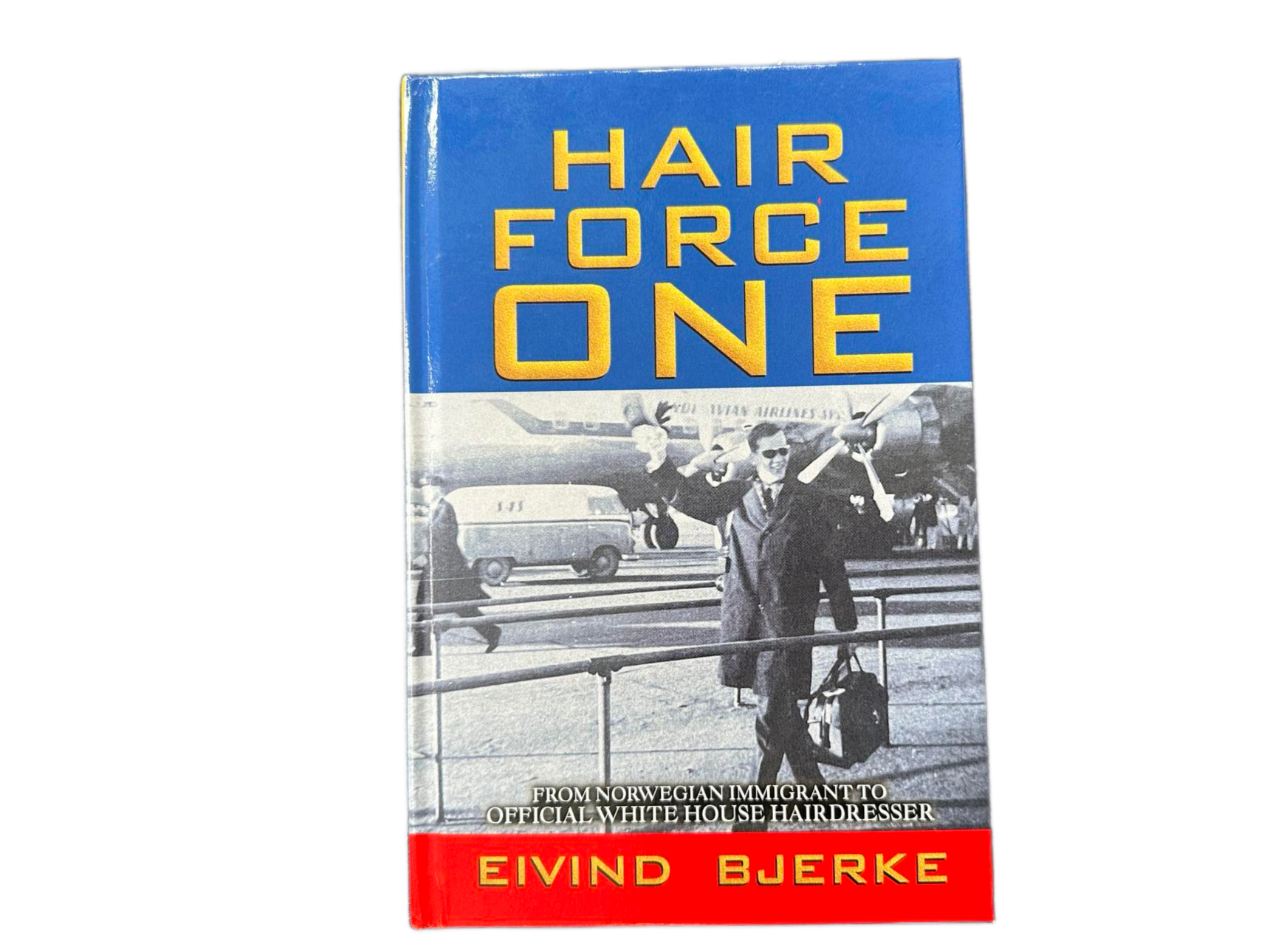 Red and Blue Hardback Book cover of Hair Force One wth black and white image of young Eivind Bjerje walking with luggage with airplane in background. (Photo: Bjerke Collection)