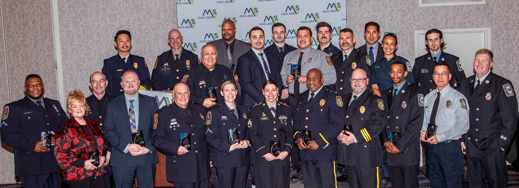 Men and women in police uniform gathered in two rows looking and smiling at camera.