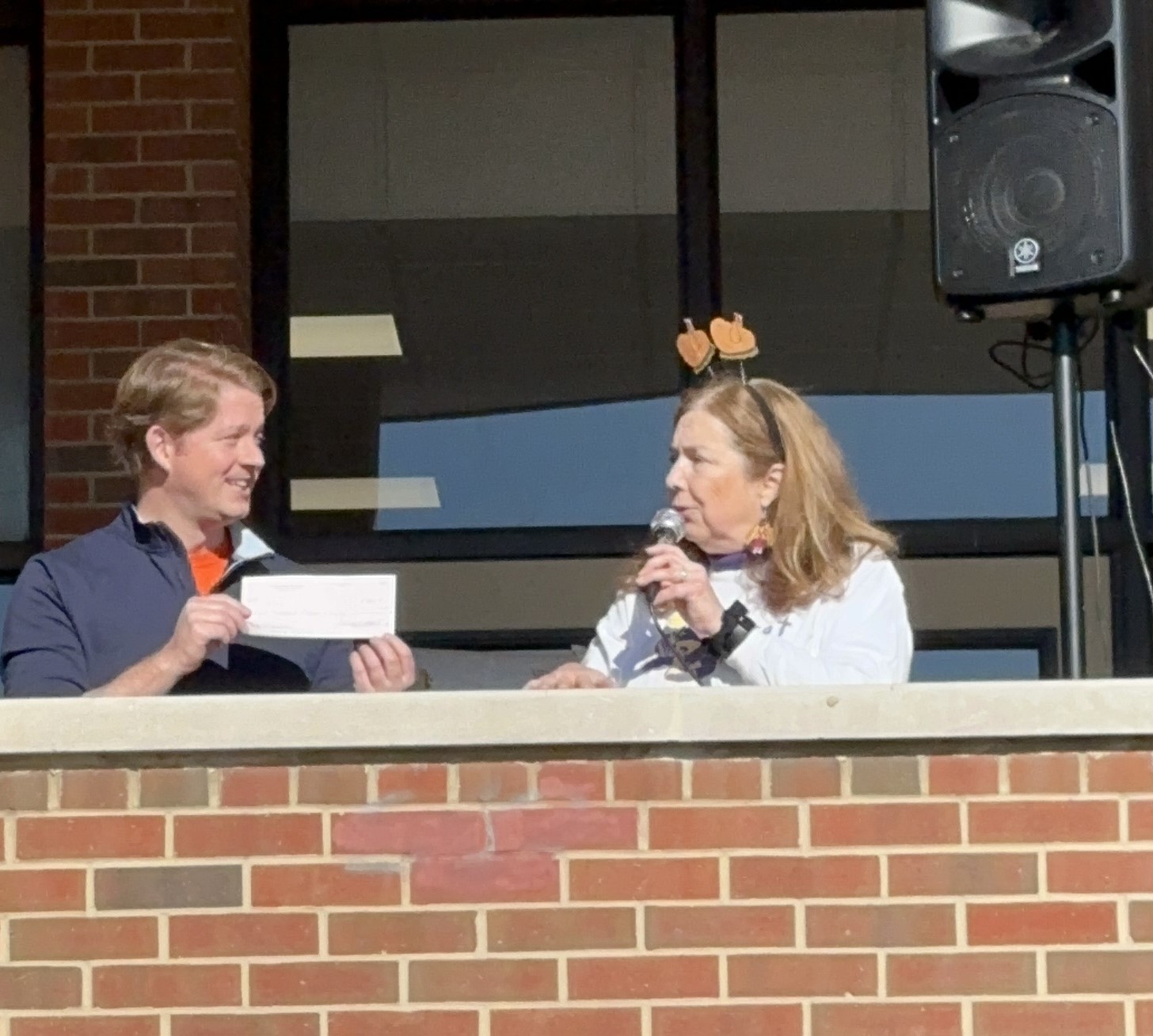 A seated man and lady talking with microphones above the gathered crowd. at the Alexandria turkey Trot.