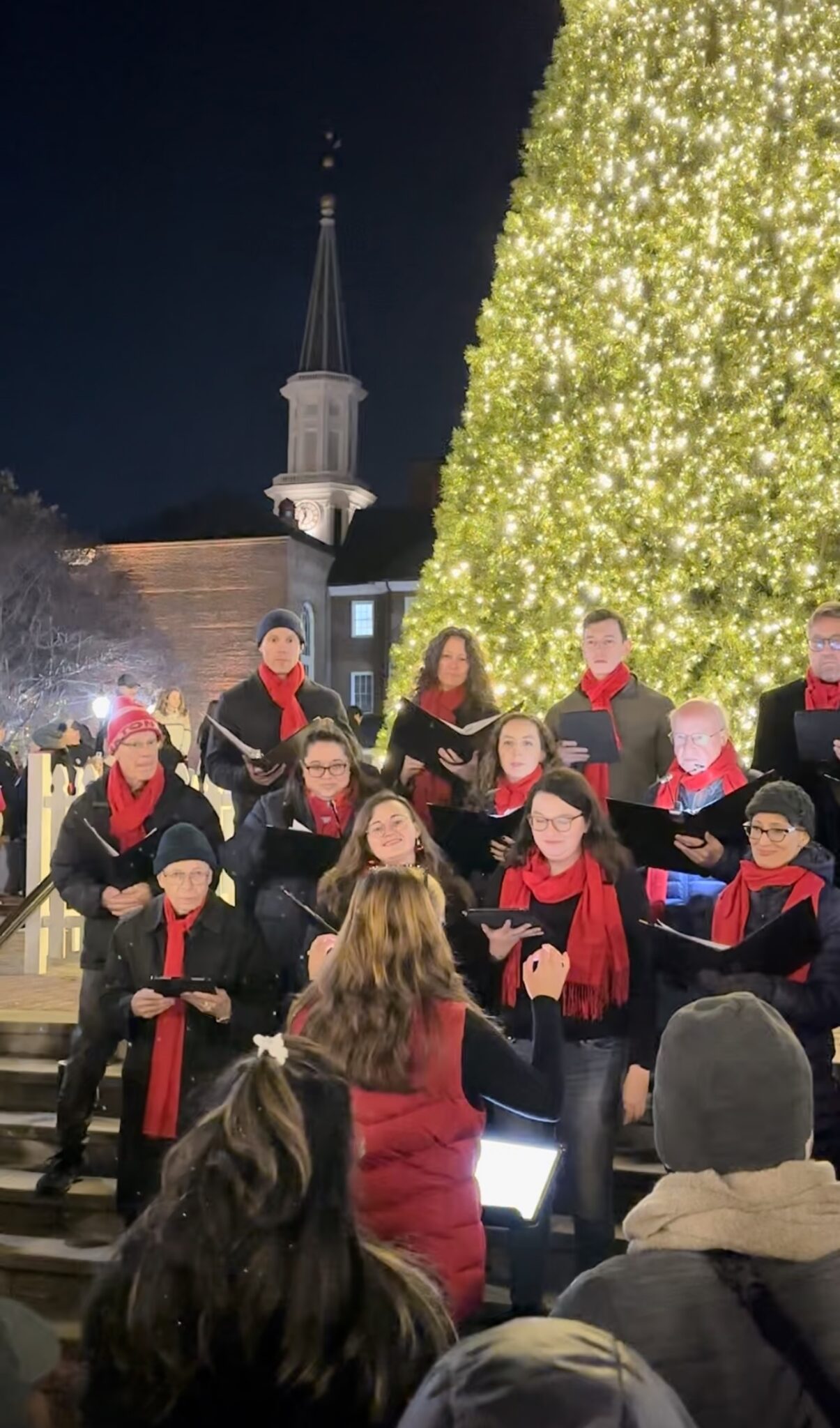 Choir sings outside in front of a Christmas tree.