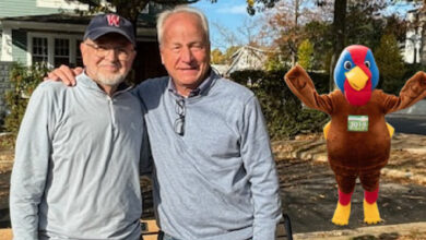 Two men arm on arm with a giant turkey mascot behind them.