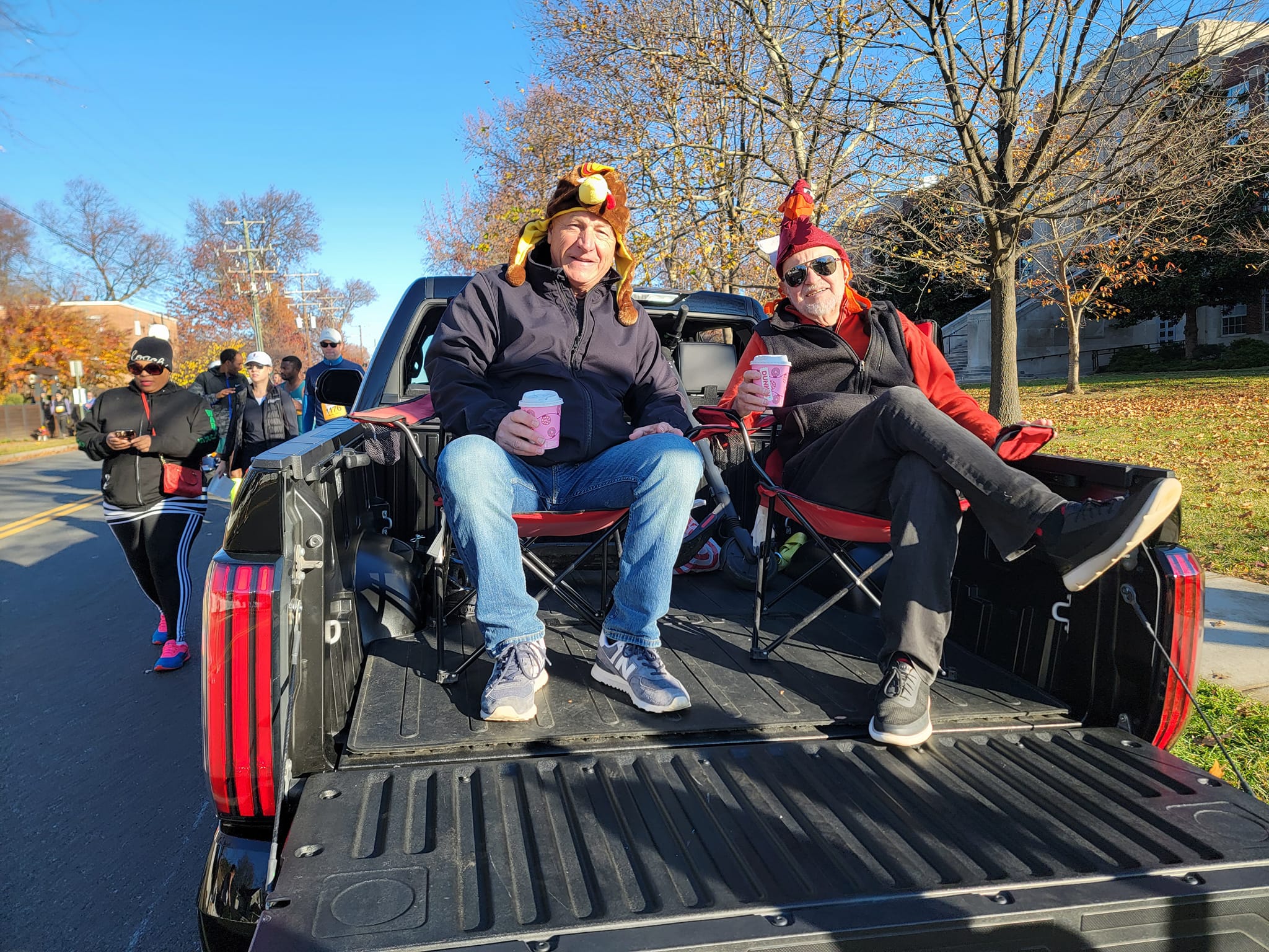 Two men wearing turkey hats sitting in back of a pickup truck.