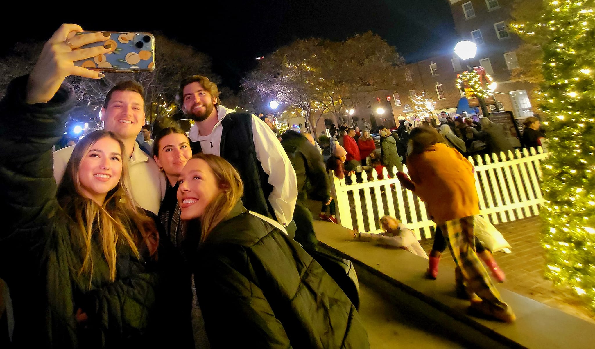 Group of five gather around camera for a selfie with Christmas tree in background.