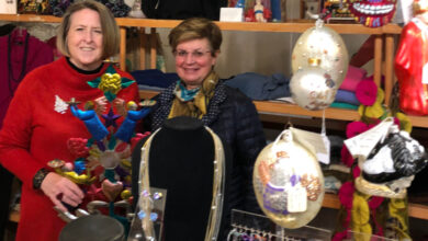 Two ladies in a store filled with colorful clothing holding a colorful candelabra at Gossypia Boutique.