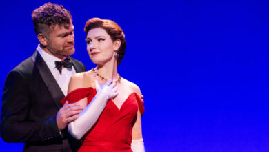 Man in suit, embracing woman in red shoulderless gown.