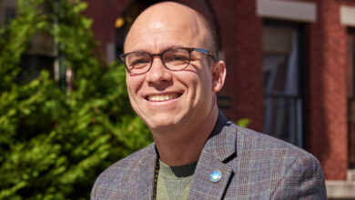 Caucasian man smiling in blazer and tee shirt.