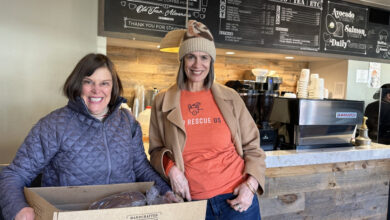 Two women facing camera holding a cardboard box full of donated food.