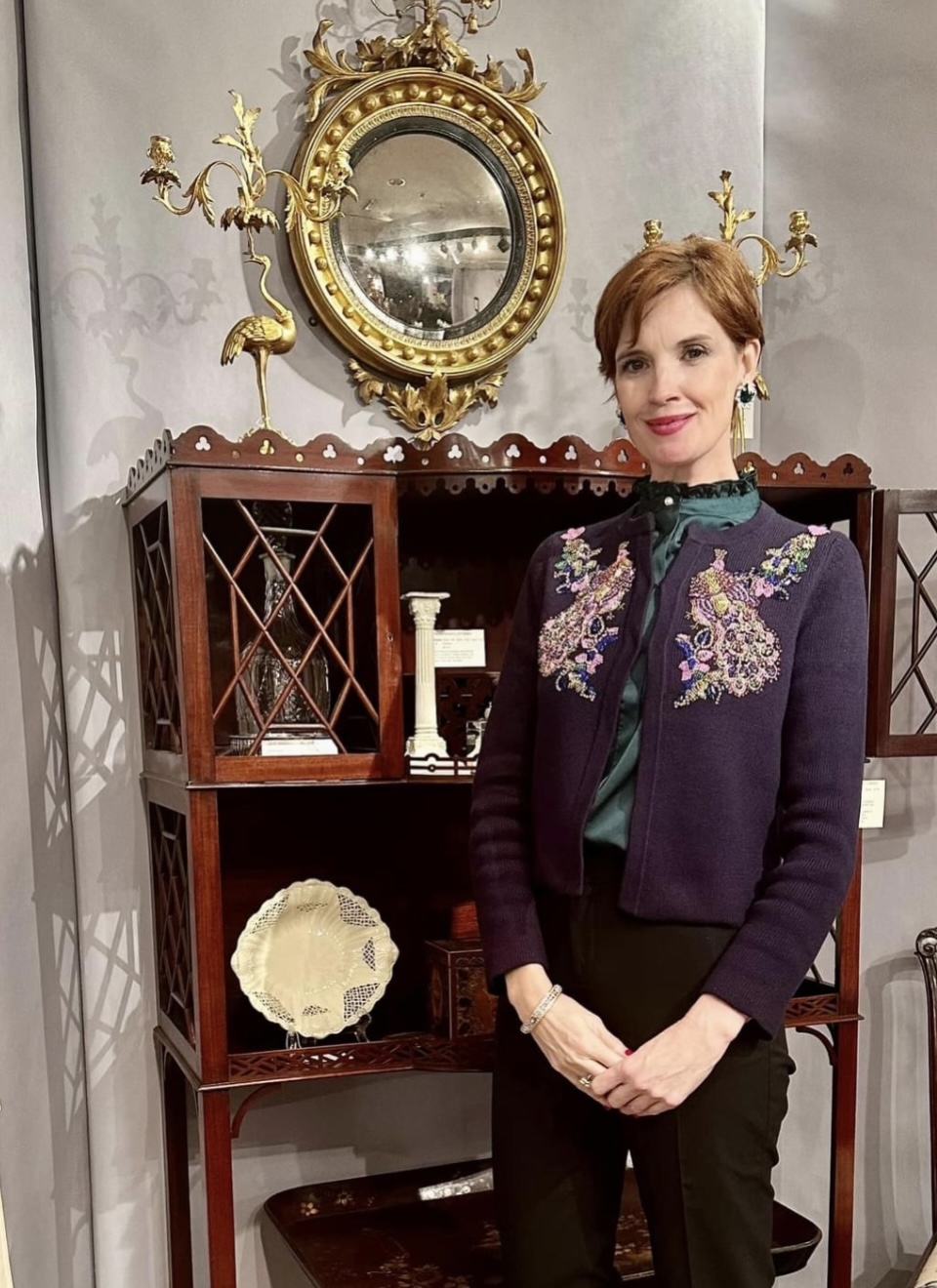 Well dressed woman in front of an antique cabinet and mirror.