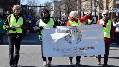 Four people in a parade carrying a big banner that says Volunteer Alexandria .