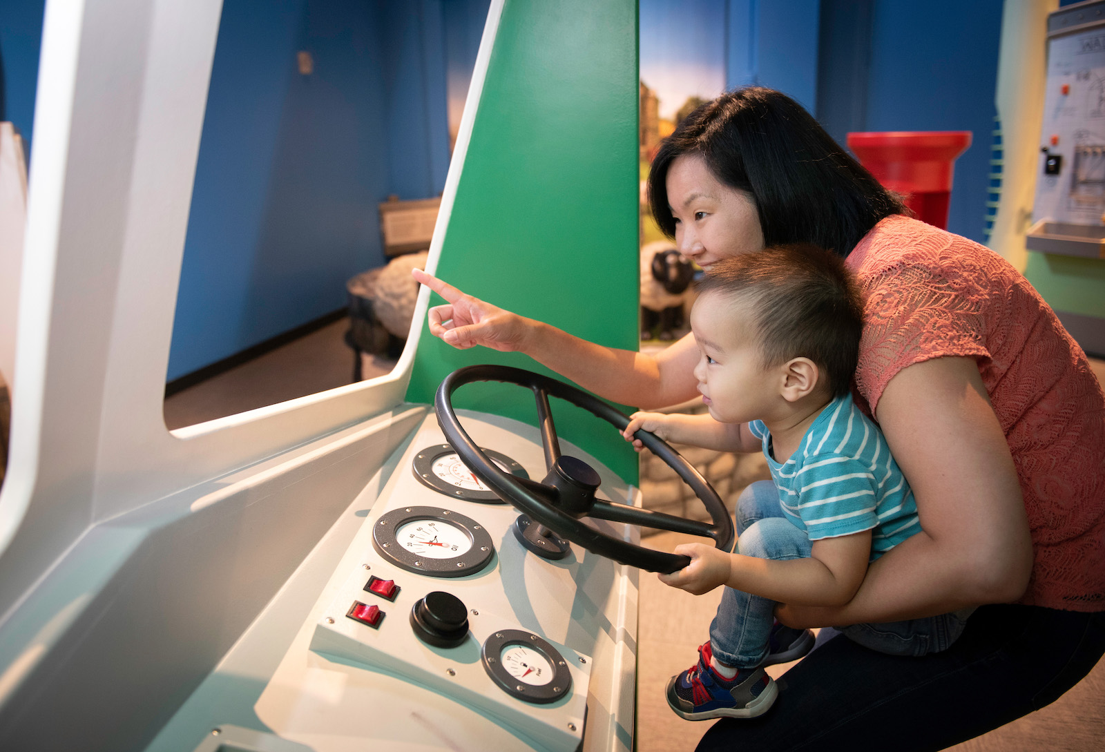 a toddler and his mother at a steering wheel driving exhibit.