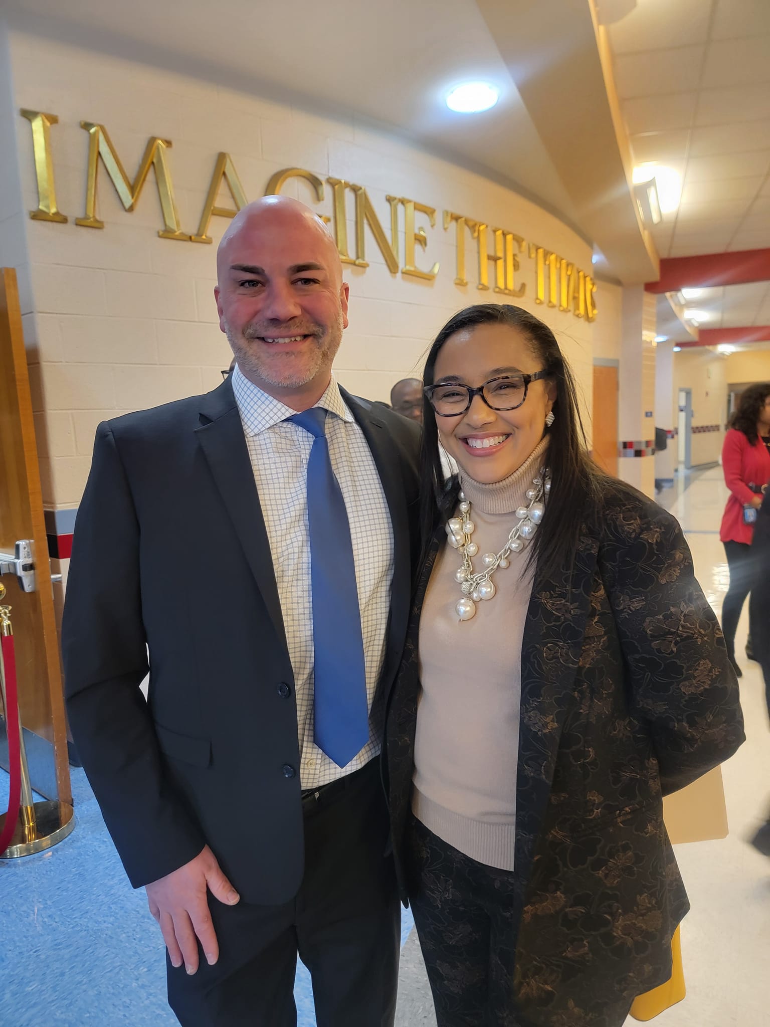 A man and woman pose together in a school hallway