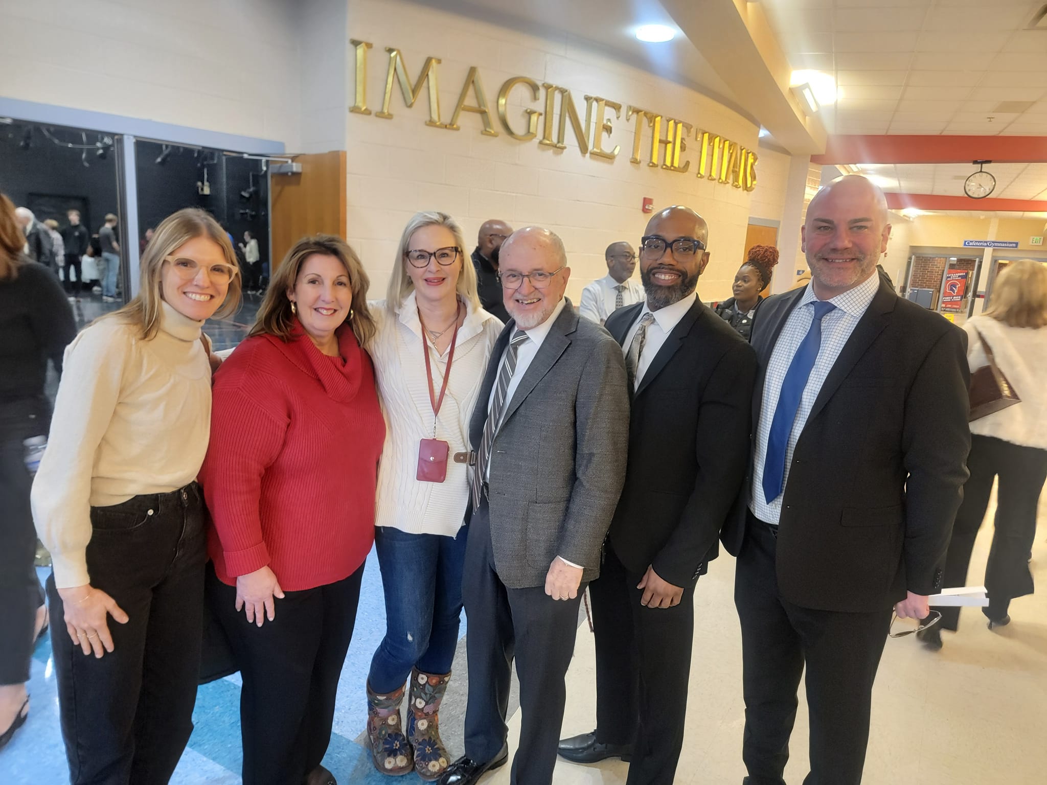 A group of educators pose for camera in school hallway.