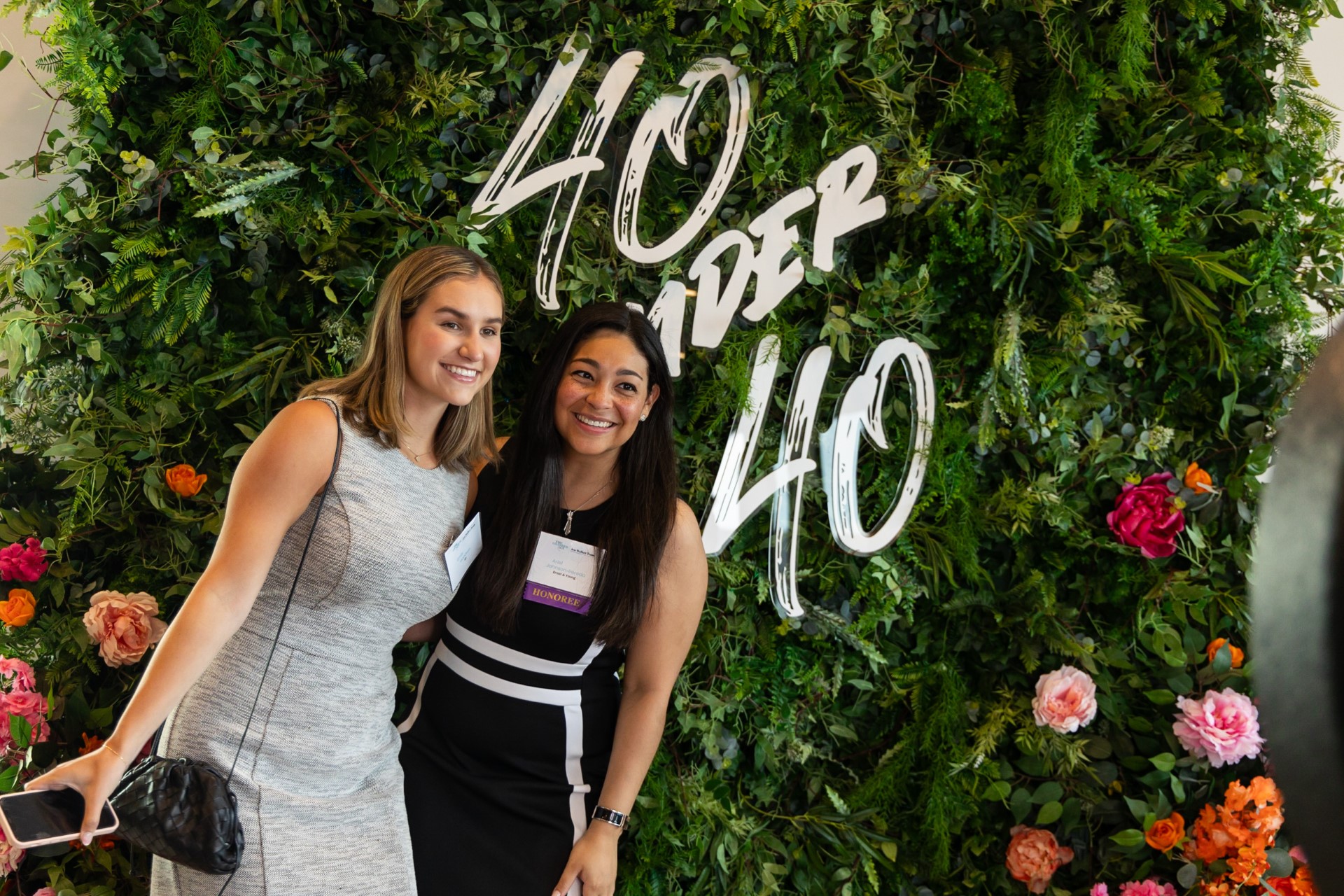 Two pretty female professionals posing by a 40 under 40 sign