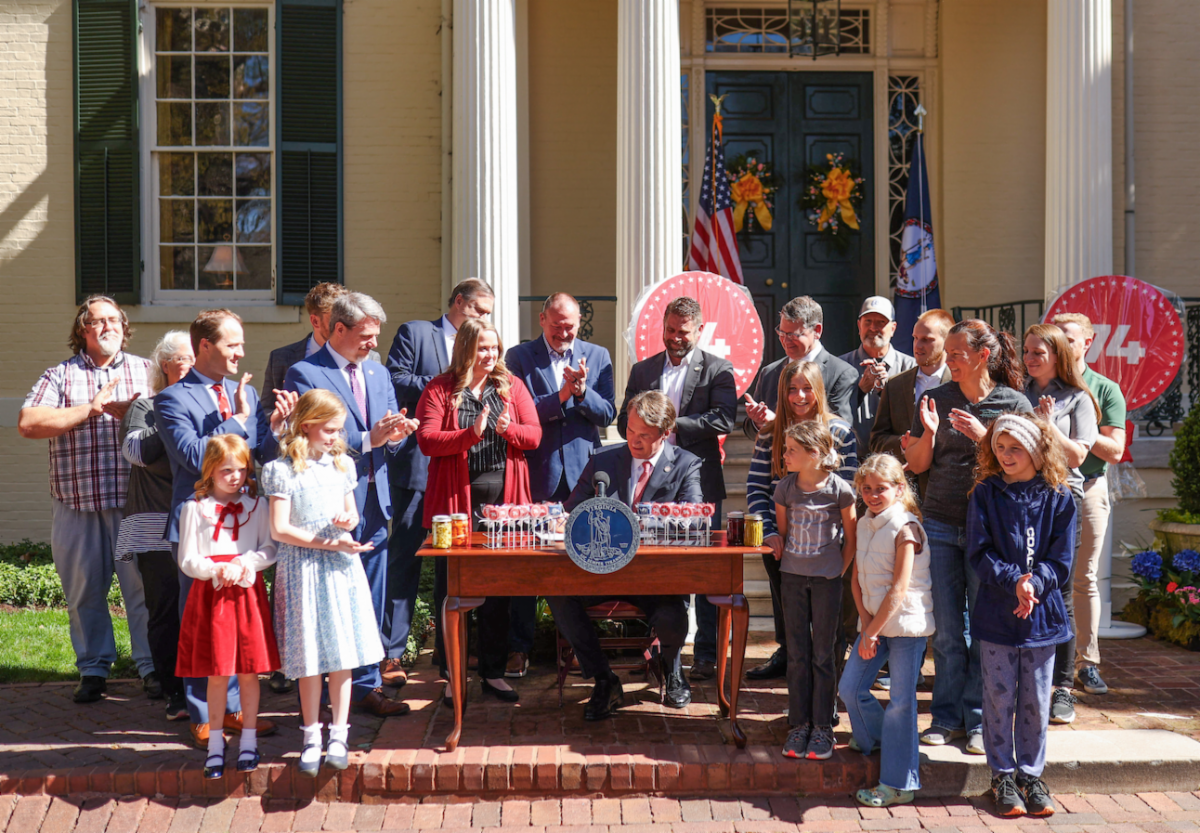 Governor surrounded by large crowd with desk covered in cake pops, signs new cake pop law in Virginia.