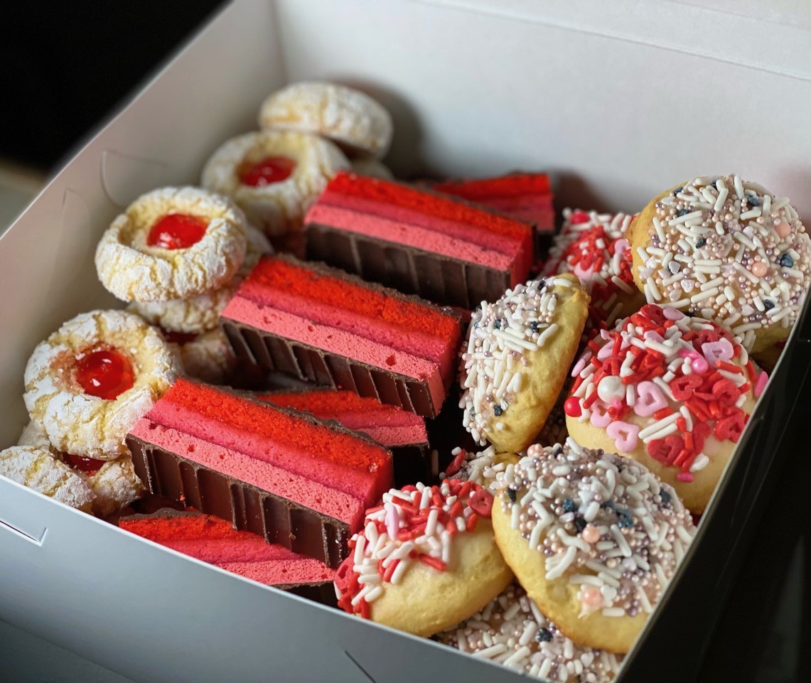 Box full of brightly colored baked cookies and small cakes.