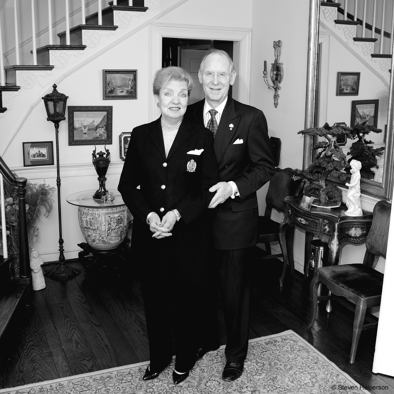 Older couple in black and white by their staircase. 