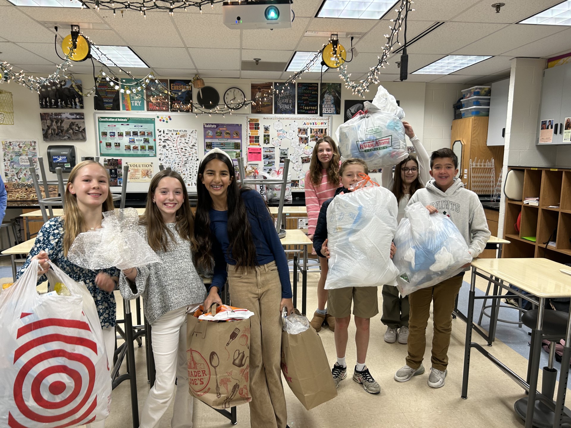 Group of middle school students smiling and holding big plastic trash bags full of recycled plastic.