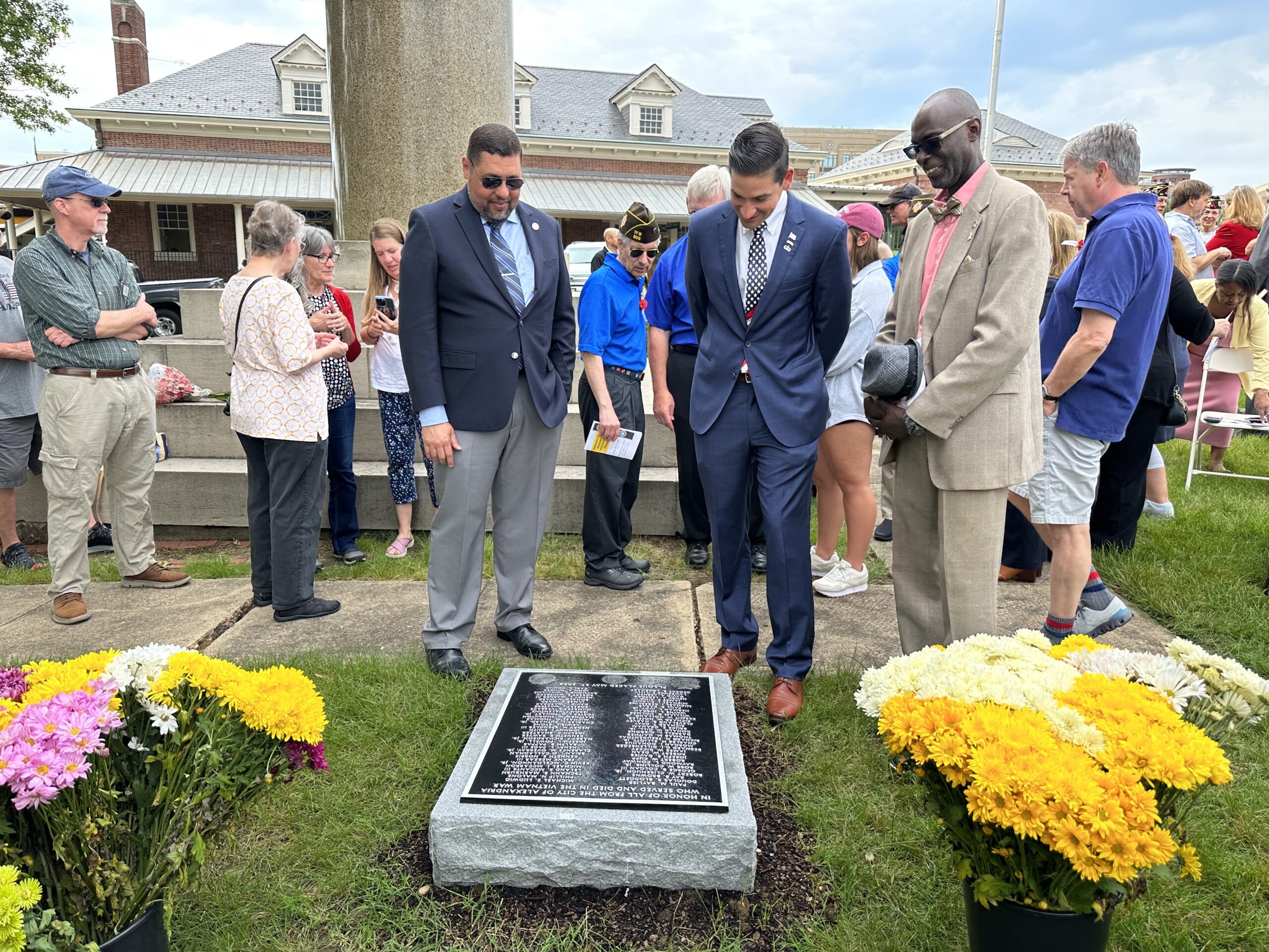 people standing and talking and a few staring down at a bronze plaque set in stone