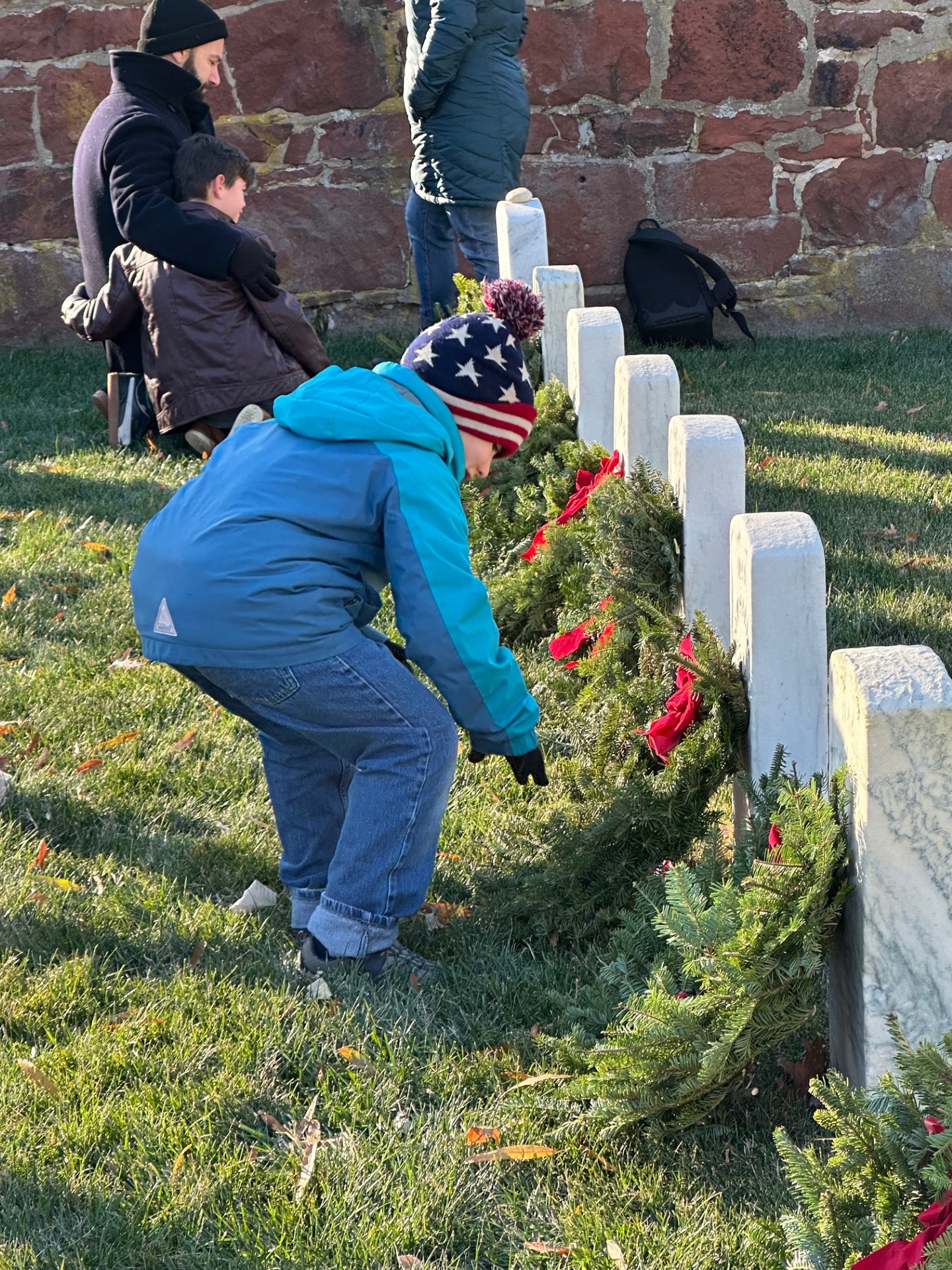 Little boy adjusts wreath at a grave markery