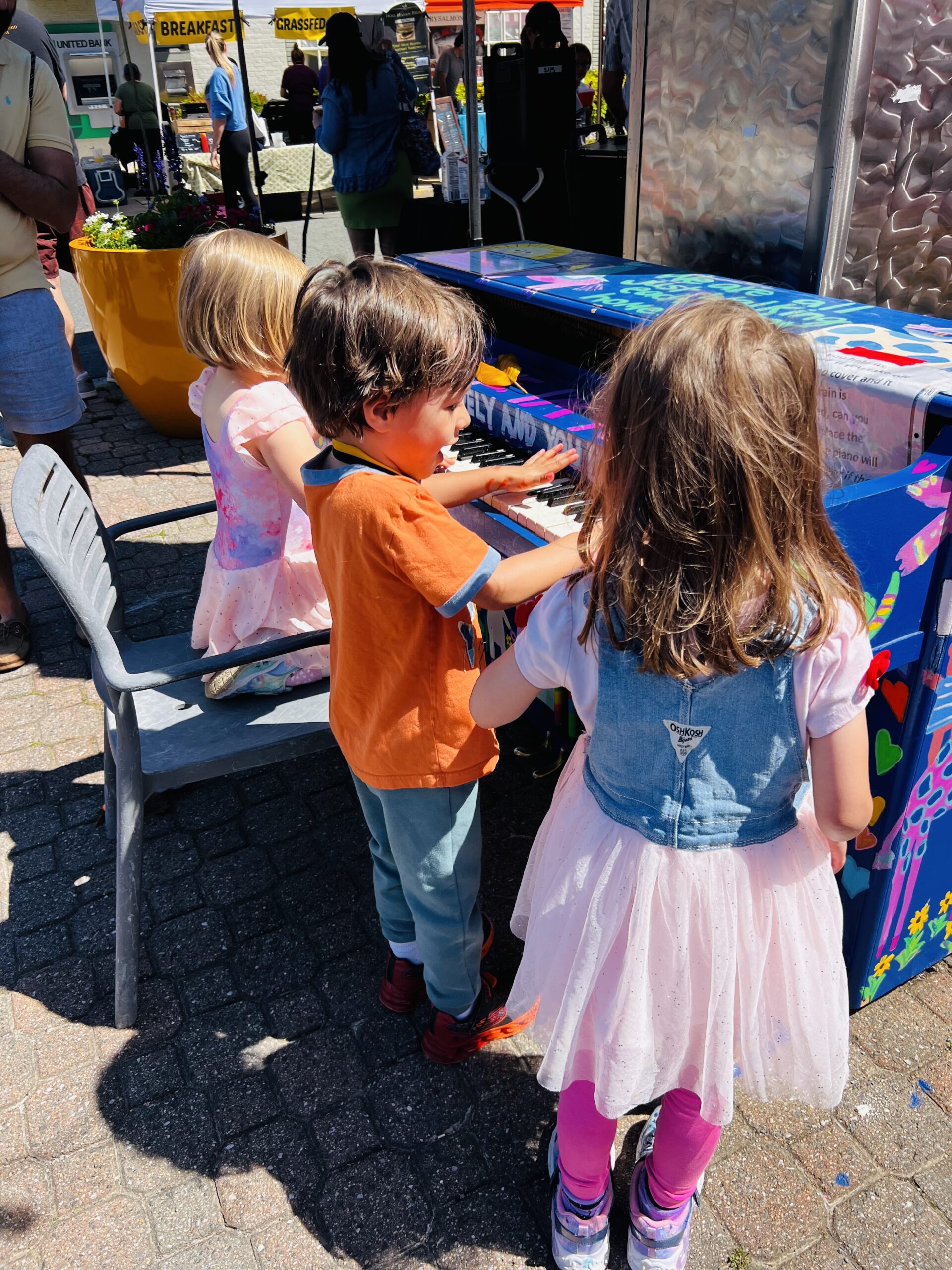 While parents browse the market, children find joy in playing the colorful piano, a fixture that both encourages community interaction and honors local creativity. This instrument is a revolving canvas for the arts, regularly refreshed with new designs by local talents including Kristin Neubauer, Margaret Wohler, Vanessa Vale, and students from George Washington Middle School.