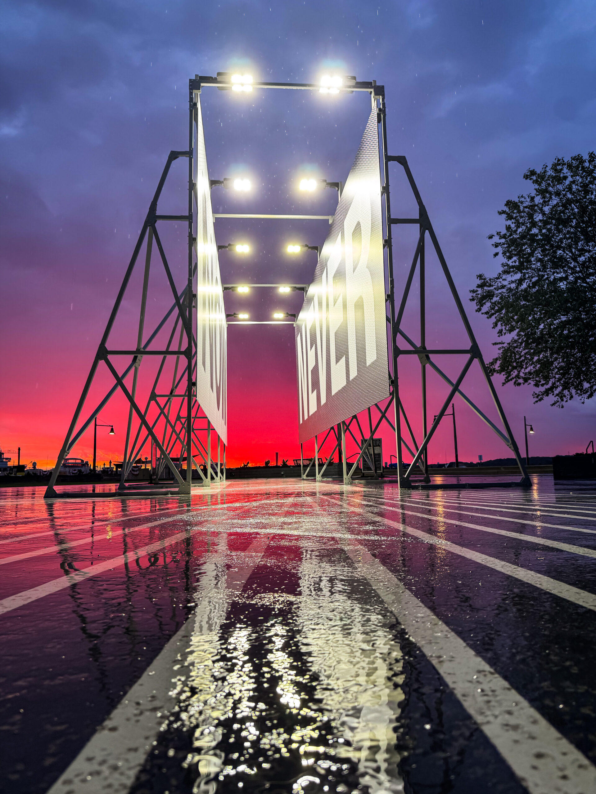 Summer Solstice Dawn at Now or Never Alicia Eggert's Now or Never installation stands illuminated at Alexandria's Waterfront Park as a brilliant red and purple dawn sky reflects off rain-soaked pavement on the morning of the Summer Solstice.