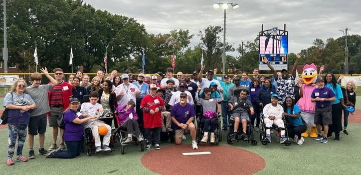 A large group of Miracle League of Alexandria players, volunteer buddies and supporters pose together around home plate.