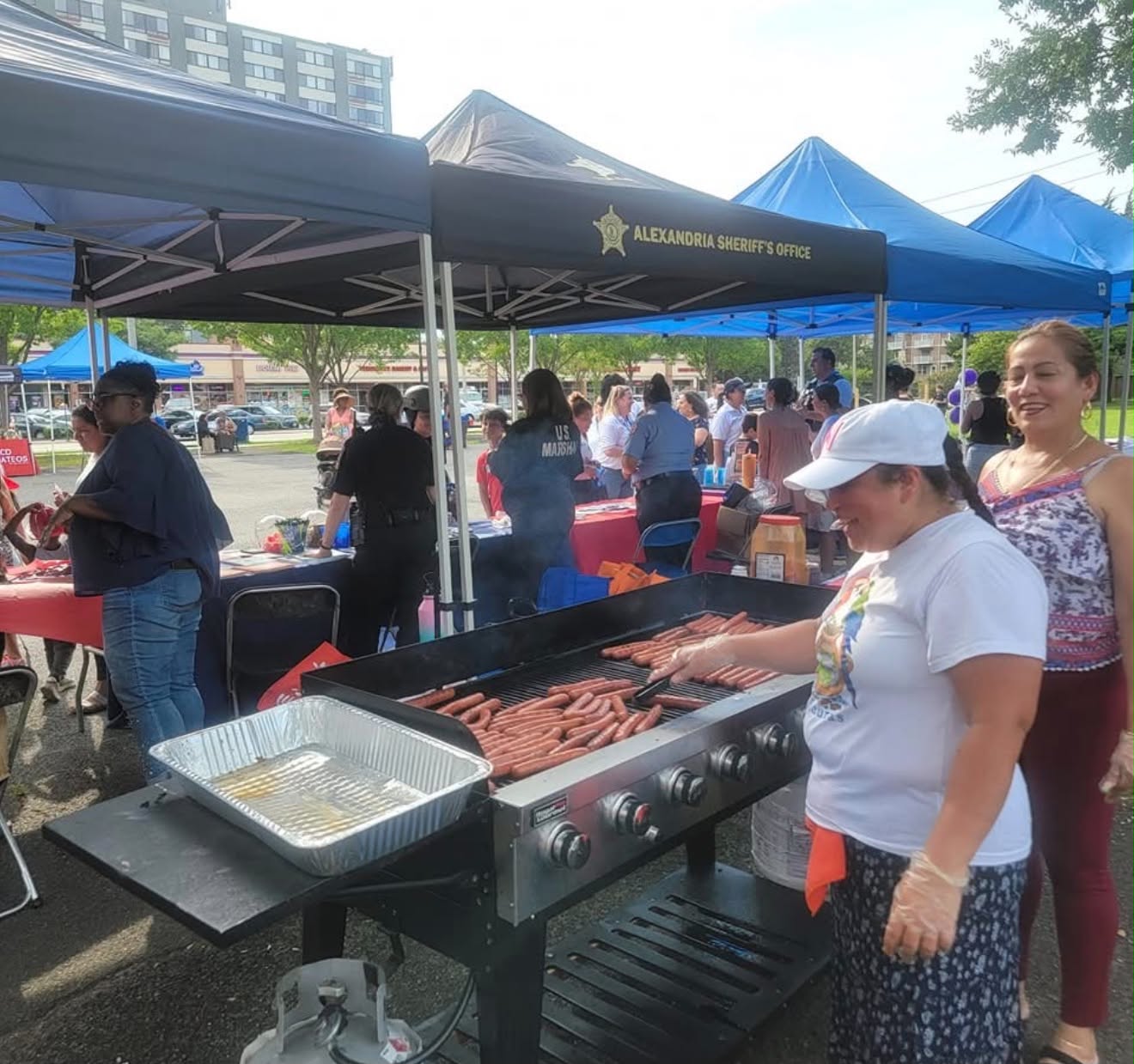 Volunteers grill hot dogs while residents visit booths hosted by public safety agencies during a National Night Out celebration in Alexandria.