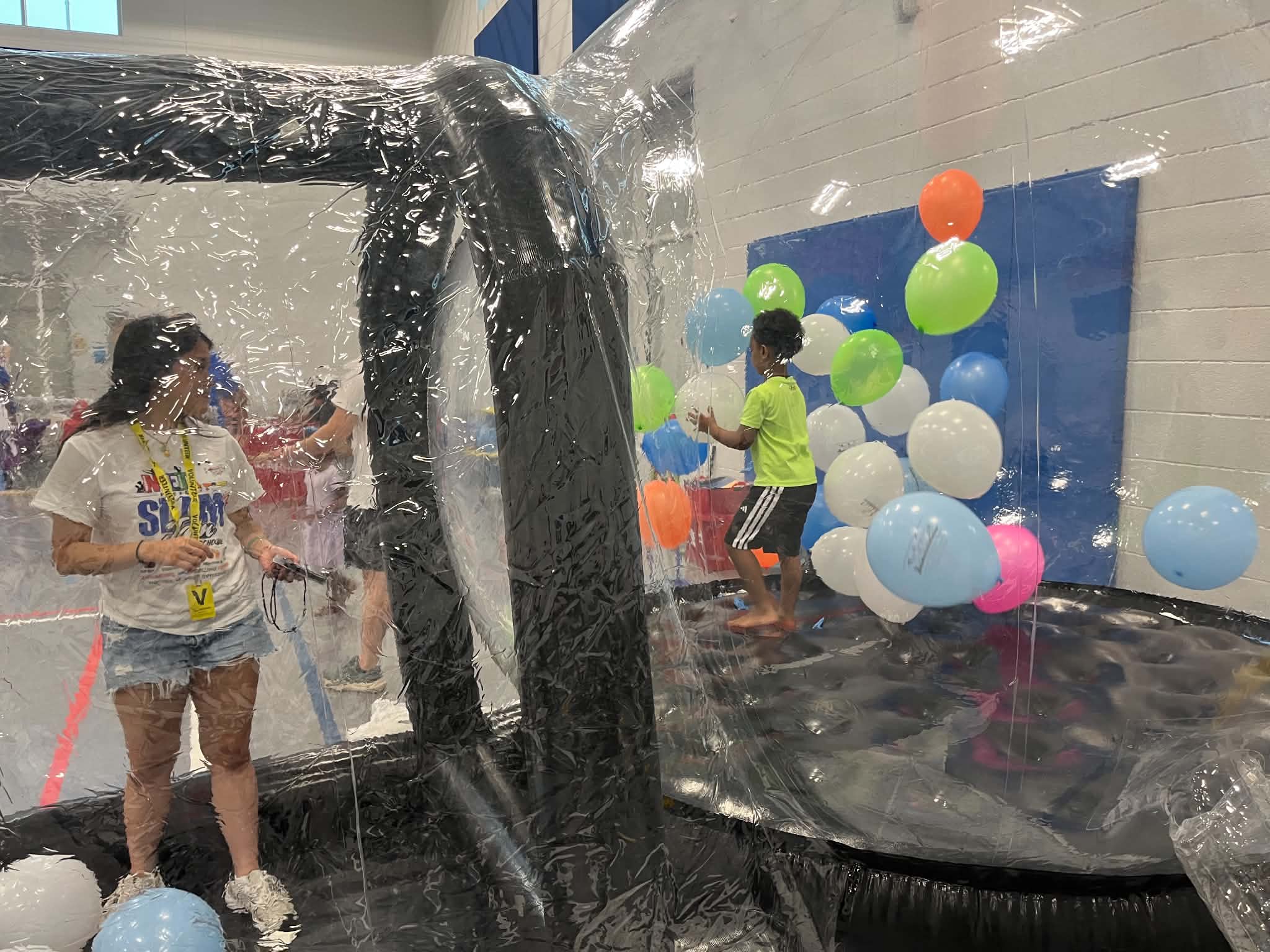 Volunteer Natalie Thai watches Lucas Baye, 5, play in a clear inflatable bounce house surrounded by colorful balloons at the METWC Back 2 School Slam Jam.