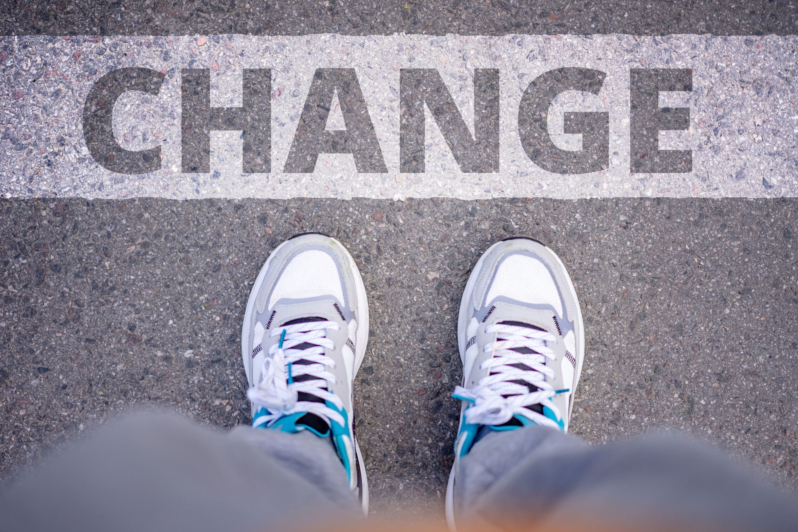 Person wearing white sneakers stands beside the word Change painted on a street.
