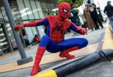 Cosplayer Cyan Blur crouches in a red-and-blue Spider-Man costume beside a curb.